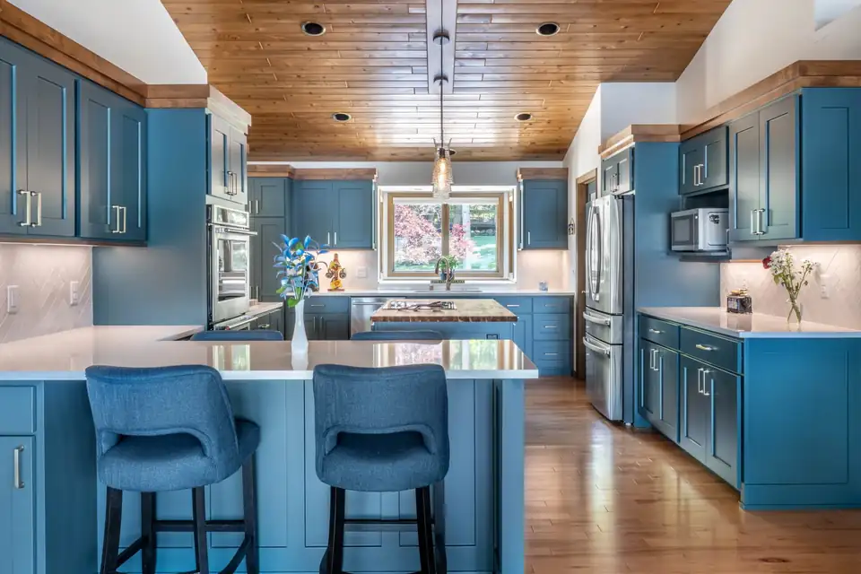 Kitchen remodeling Madison WI area: Lake Wisconsin kitchen with blue shaker cabinets, blue island stools, quartz counters and a knotty pine ceiling