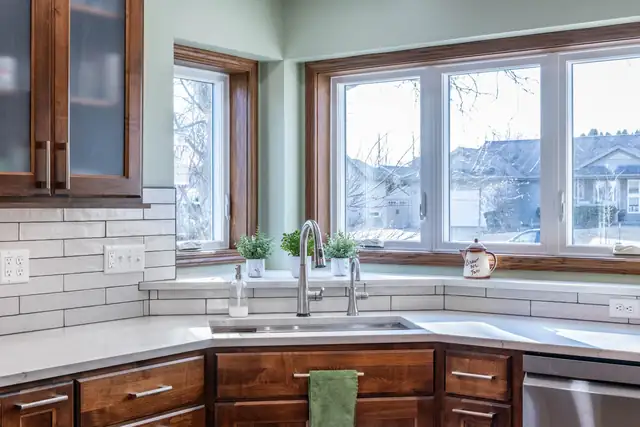 Kitchen remodel in DeForest, WI with wood cabinets, white subway tile, quartz counters and a corner sink under three windows