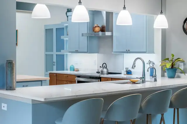Brooklyn, WI kitchen with pale blue cabinets, a white quartz peninsula, white pendants and gray counter stools