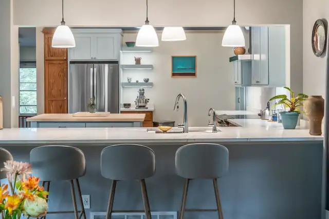 Coastal kitchen remodel in Brooklyn, WI with white pendants, slate-blue peninsula, gray stools and open shelving